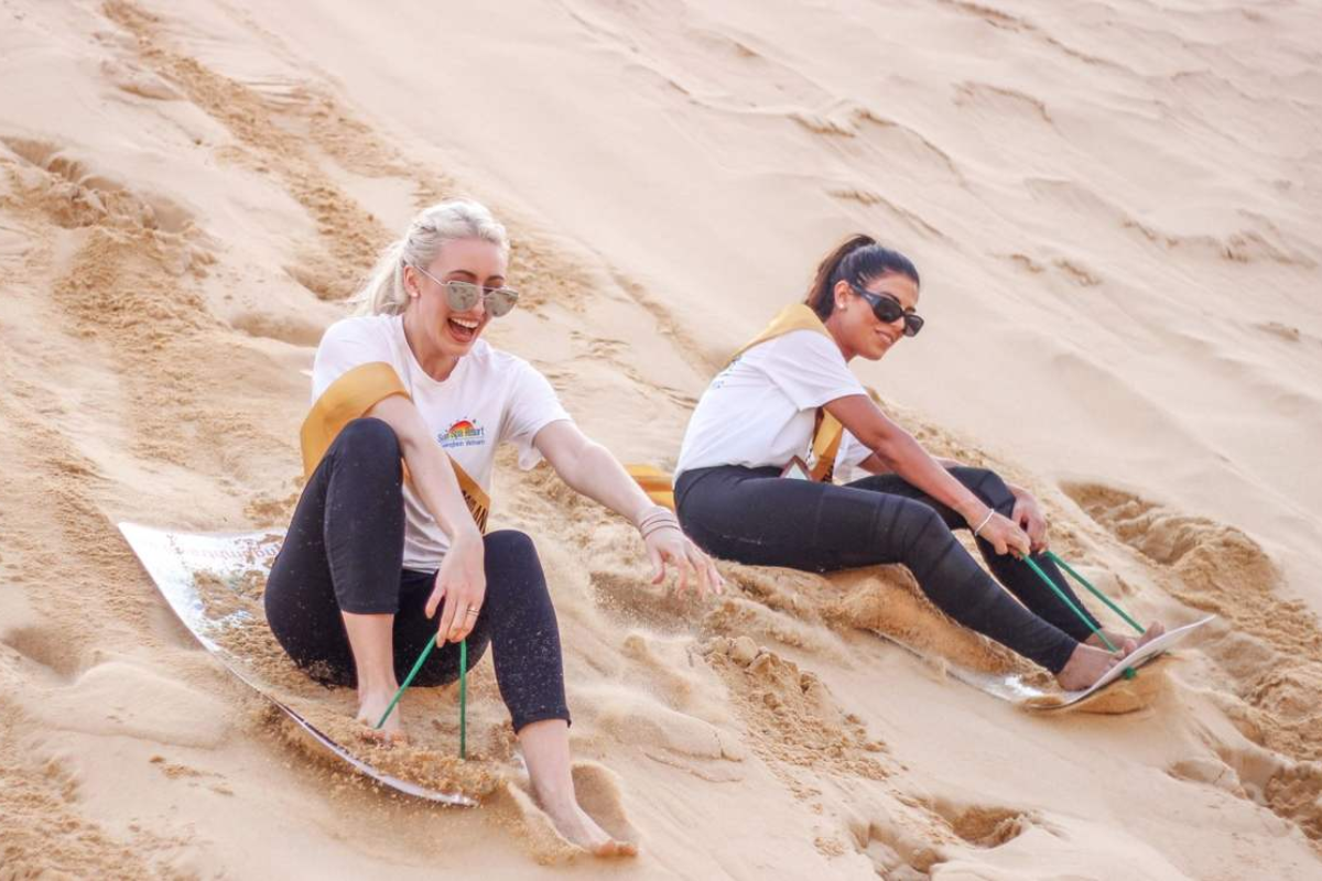 Tourist enjoying sandboarding down a steep white sand dune at Bau Trang